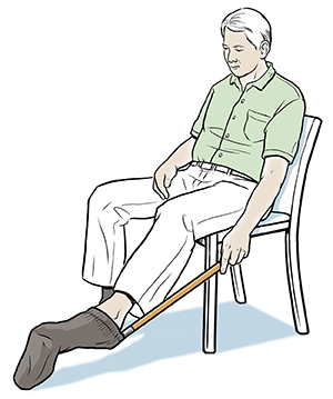 Seated man using long-handled sock donner.