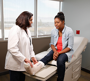 Healthcare provider examining cast on woman's leg.