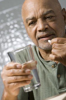 Man putting a pill in his mouth with one hand and holding a glass of water with the other hand.