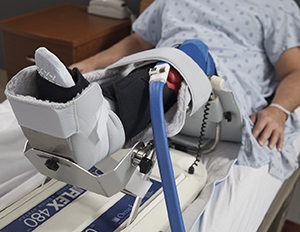 Man in hospital bed with leg in continuous passive motion machine.