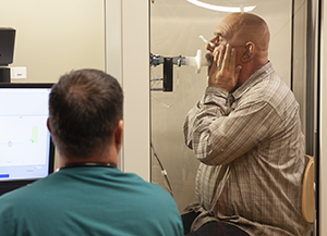 Technician performing pulmonary function tests on man in testing booth.