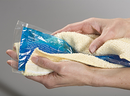 Primer plano de manos envolviendo una compresa de hielo en una toalla.