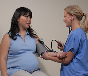 Proveedora de atención médica midiéndole la presión arterial a una mujer embarazada