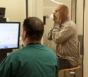 Un técnico le realiza pruebas de función pulmonar a un hombre en una cabina de prueba.