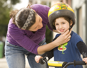 Mujer que le coloca un casco a un niño de edad preescolar que anda en bicicleta.