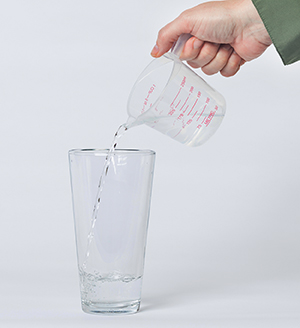 Una mano vierte agua de un medidor a un vaso.