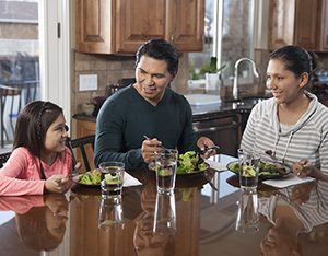 Hombre, mujer y niña comiendo una comida saludable en su casa.