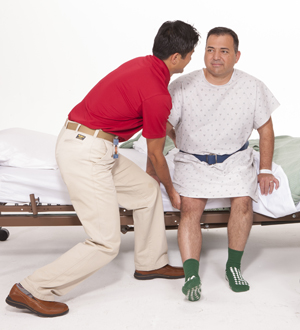 Physical therapist helping a man out of a hospital bed.