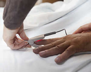 Closeup of healthcare provider's hands putting pulse oximeter on man's finger.
