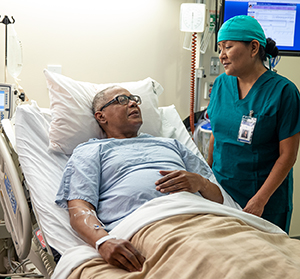 Un proveedor de atención médica habla con un hombre en la cama de un hospital.