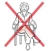 Vista frontal de una mujer sentada en una silla con las piernas cruzadas. La X roja indica que esto no debe hacerse.