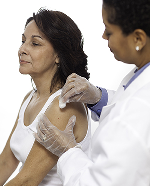Proveedora de atención médica que prepara para aplicarle una inyección en el brazo a una mujer.