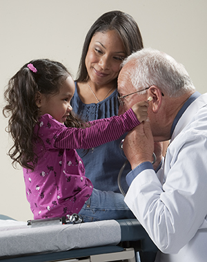 Proveedor de atención médica jugando con un estetoscopio con una niña pequeña mientras una mujer los observa.