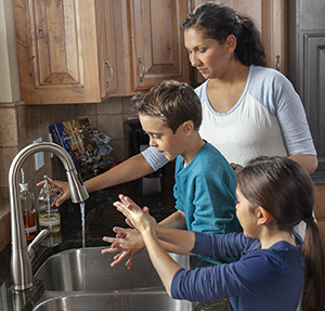 Mujer ayudando a un niño y a una niña a lavarse las manos en el fregadero de una cocina.