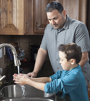 Hombre ayudando a un niño a lavarse las manos en el fregadero de una cocina.