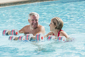 Una mujer y un hombre haciendo ejercicios aeróbicos con pesas en la piscina.