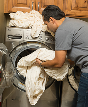 Un hombre poniendo sábanas en una lavadora de uso doméstico.