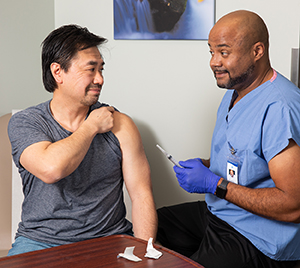Proveedor de atención médica colocando una inyección en la parte superior del brazo de un hombre en la sala de examinación.