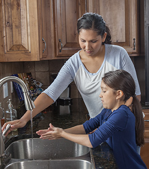 Mujer ayudando a niña a lavarse las manos en el fregadero de la cocina.